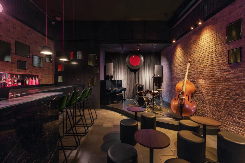 A Modern jazz bar interior design, stage with black piano and cello, lamps above bar counter promoted with venue technology.